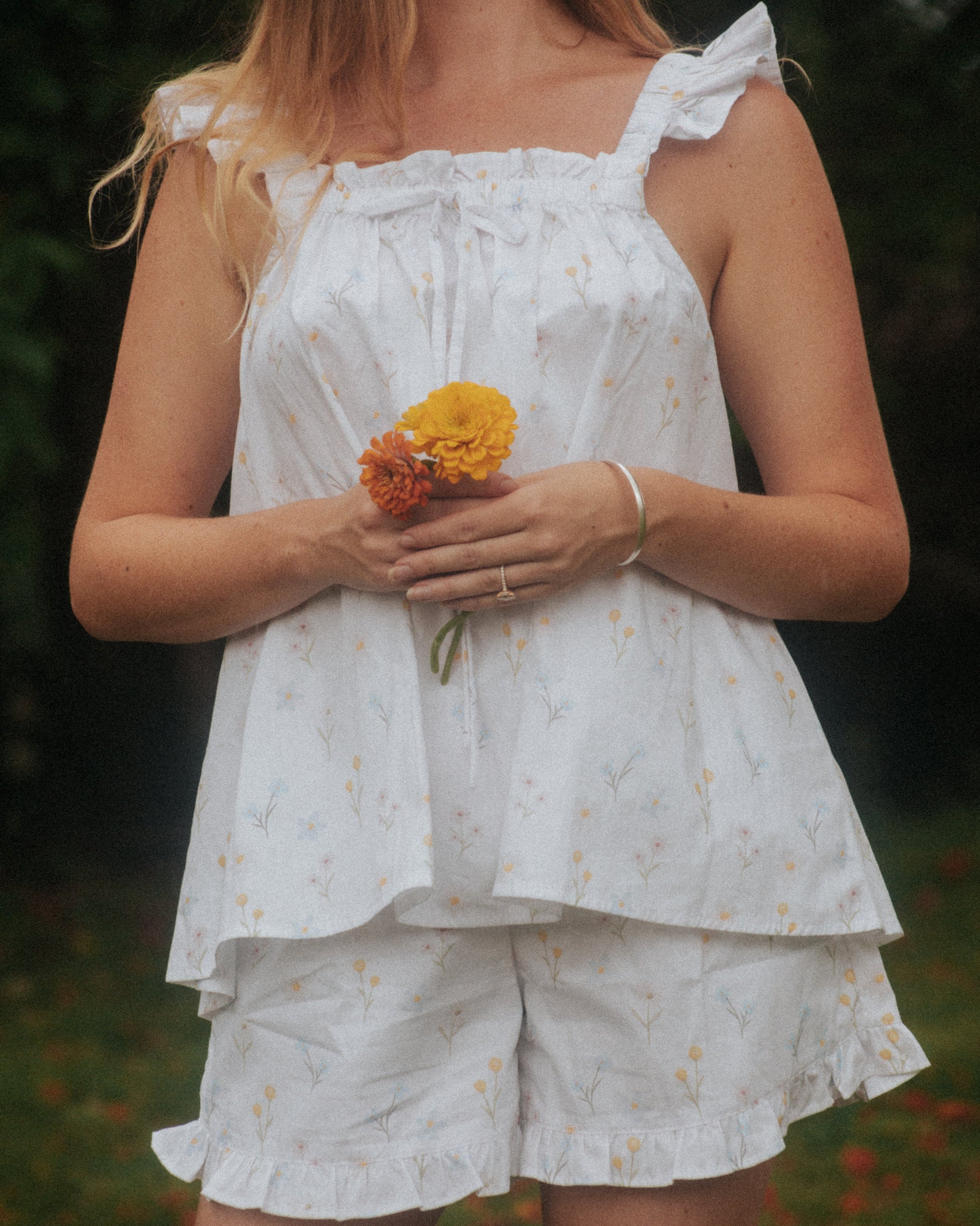 Woman wearing the Wildflower Whispers pyjama set by Simply Provincial — 100 percent cotton ruffled tank top with bow detail and matching ruffled shorts, featuring a delicate print inspired by Australian wildflowers and the native billy button bloom.