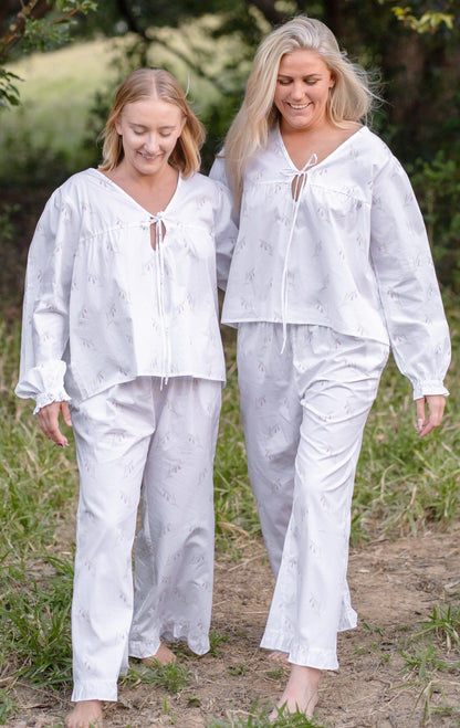 Women wearing the Heathland Bloom cotton pyjama set by Simply Provincial — handmade from cotton with long sleeves, ruffled cuffs, and soft flowing trousers. Featuring a delicate print inspired by the native Australian pink heath flower, this timeless sleepwear design captures the charm of slow living and the beauty of nature.
